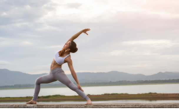 woman in crop top and tights stretching with grey sky and mountains in background